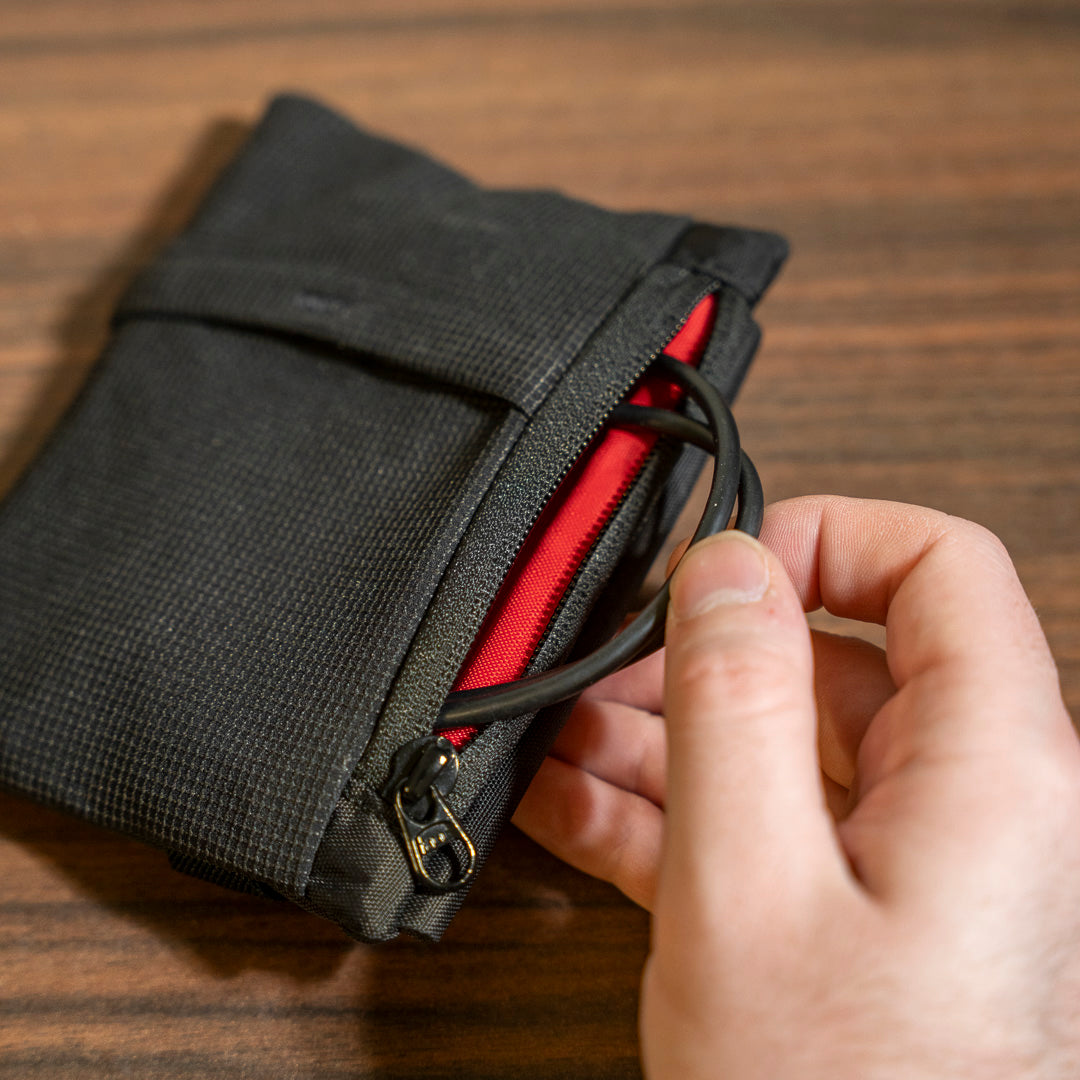 Hand opening a black zippered pouch with red interior on a wooden surface
